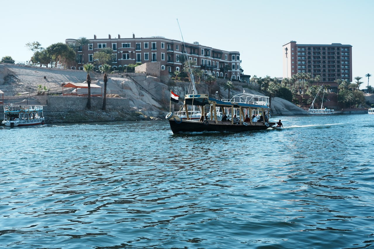 Scenic view of tour boats navigating the Nile River with architectural backdrop in Aswan, Egypt.