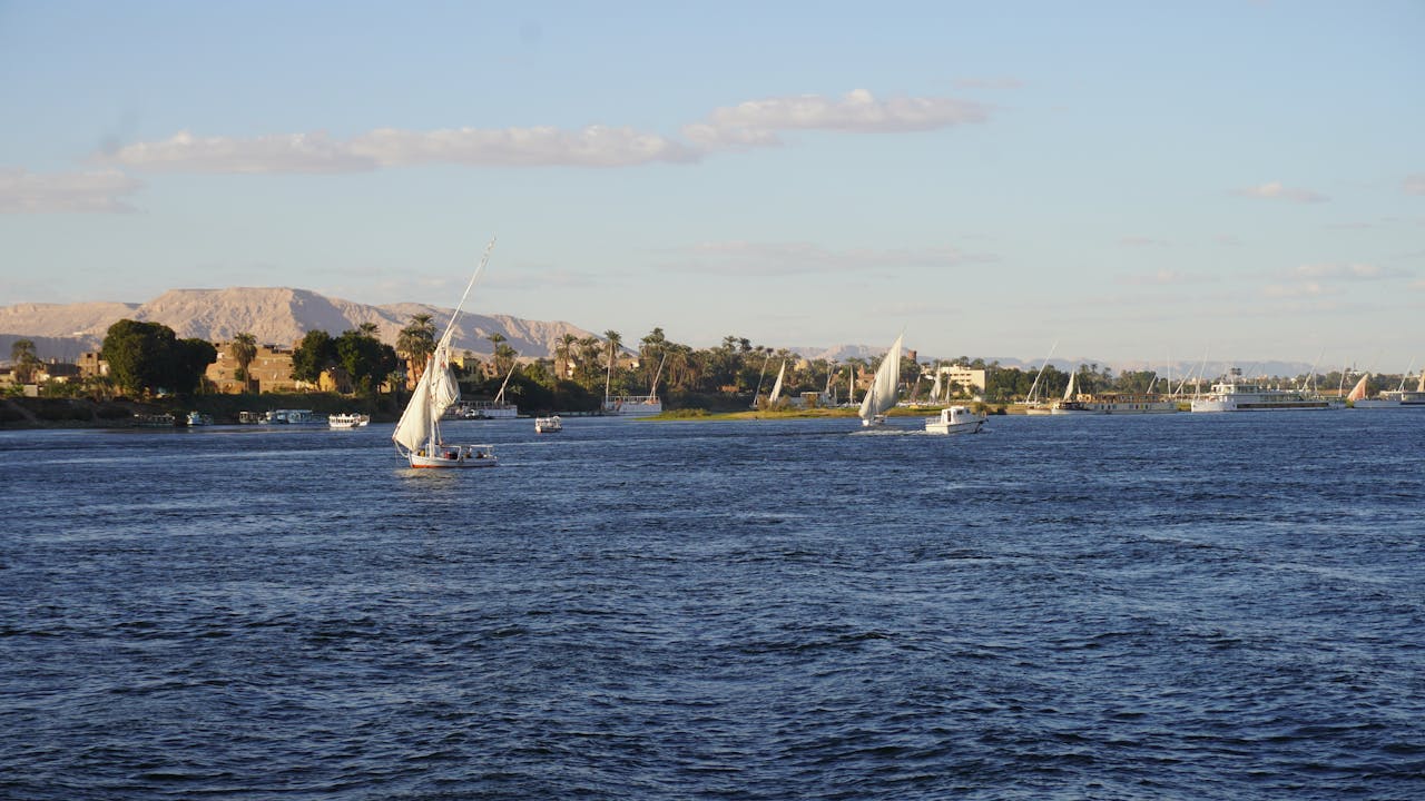 Scenic view of sailboats on the Nile with a backdrop of lush greenery and distant mountains.